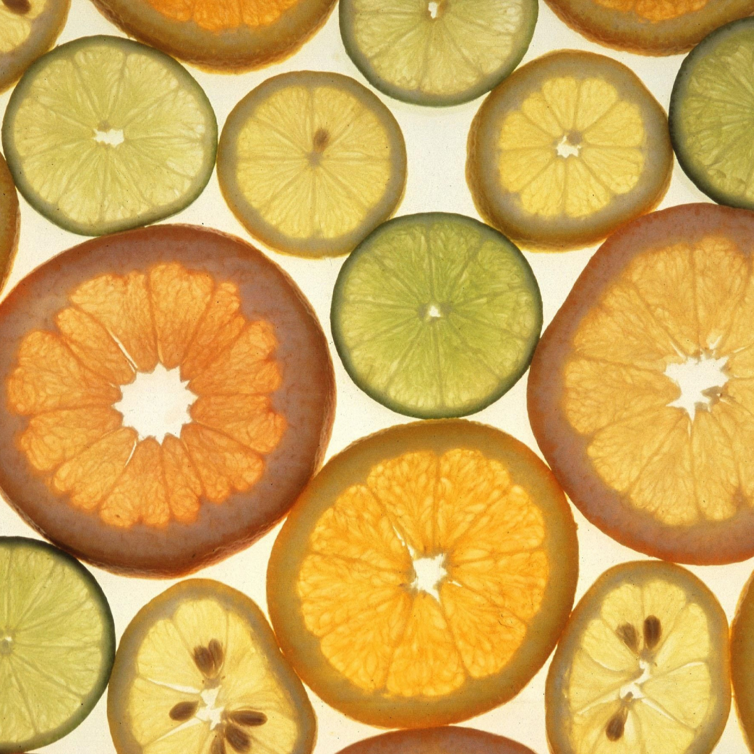 A close-up flat lay of sliced citrus fruits on a white background, including orange, mandarin, and lime wedges and cross-sections.