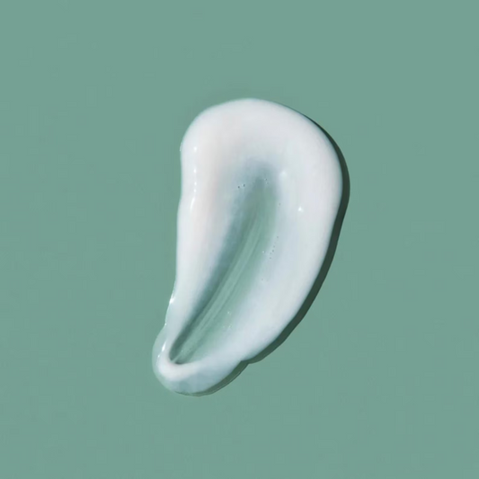 A swatch of creamy cream cleanser on a green background.