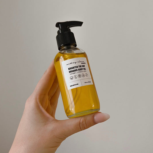 Hand holding a bottle of organic body oil with a label on a neutral background