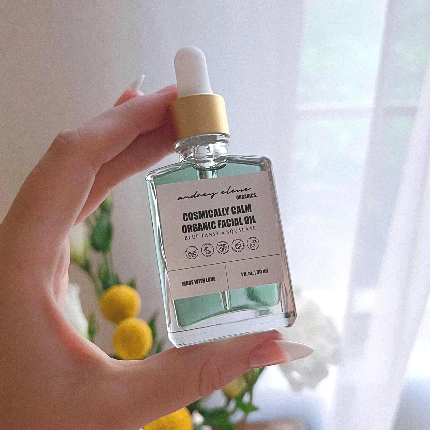 Hand holding a bottle of blue tansy and squalane organic facial oil with a blurred background